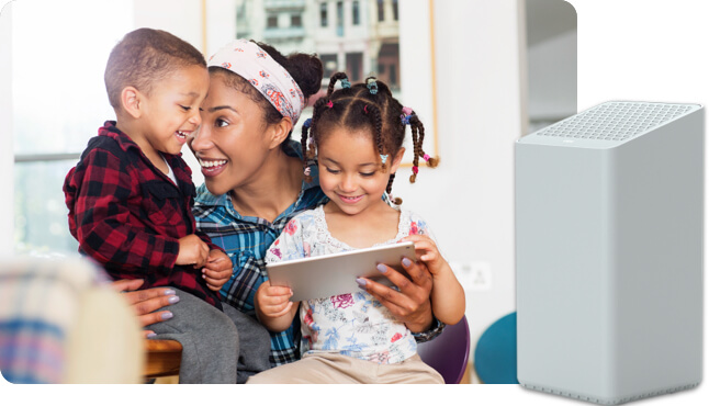 Woman with girl and boy sitting in living room looking at tablet smiling